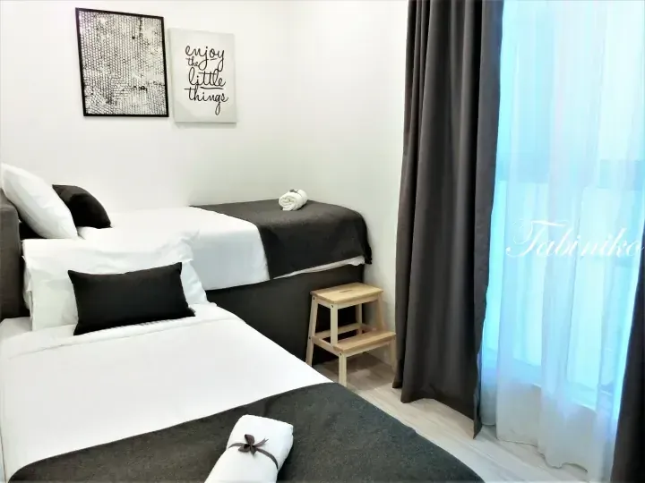 Modern bedroom with two single beds, grey curtains, and ’enjoy the little things’ wall art.