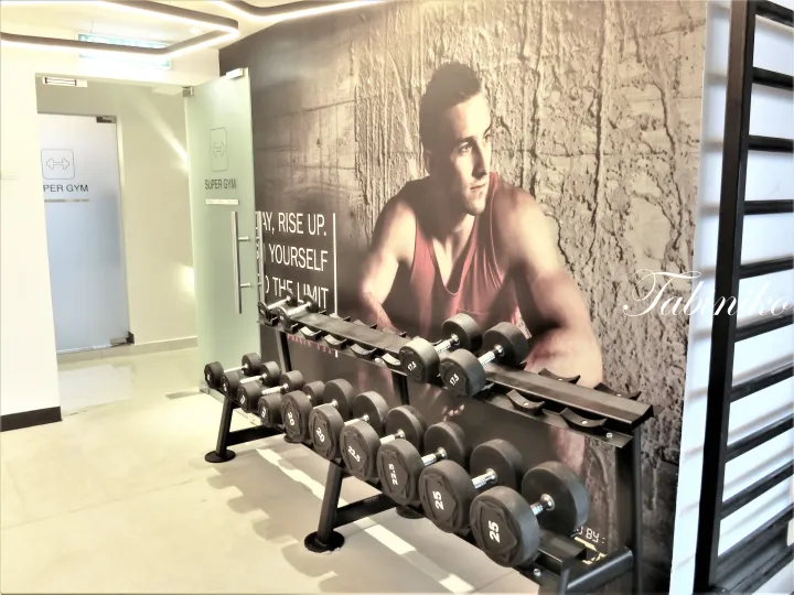筋肉質な男性の壁画と「SUPER GYM」の看板があるダンベルラック。