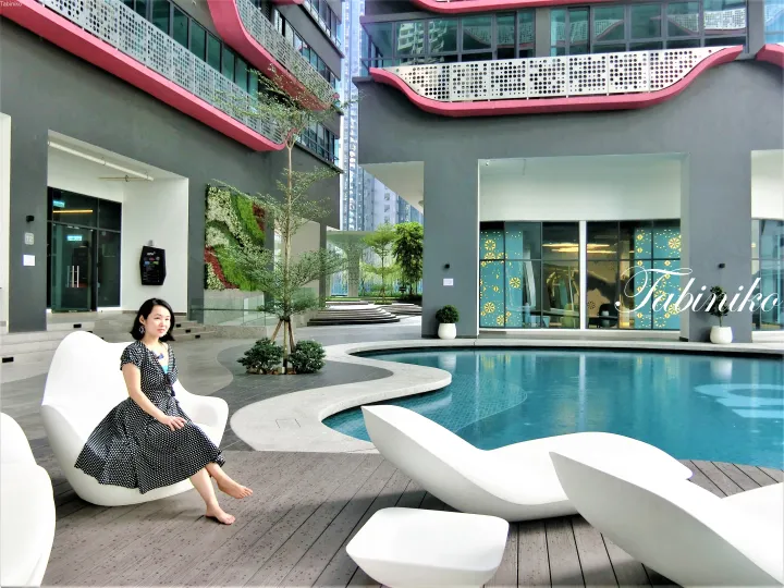 Ario+レジデンスのプールサイドで白いラウンジチェアに座る女性。