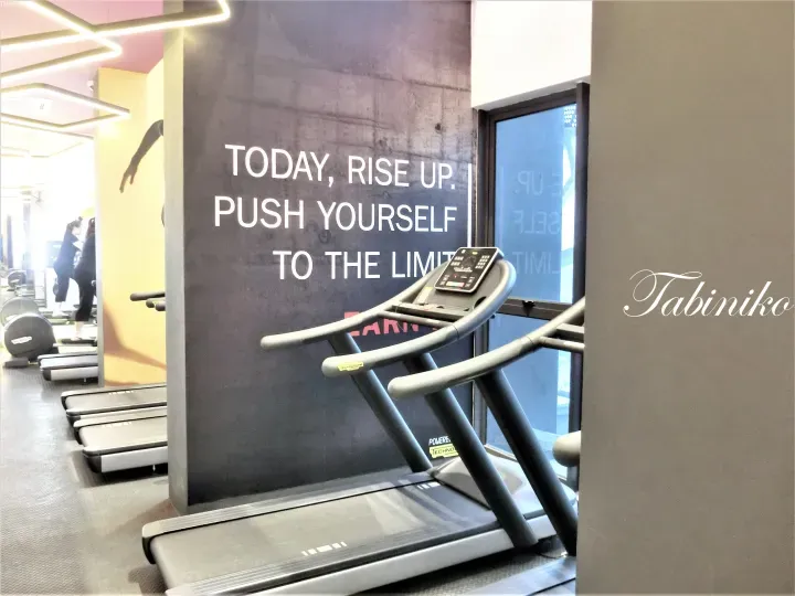 Technogym treadmill in a modern gym with motivational wall text reading “TODAY, RISE UP. PUSH YOURSELF TO THE LIMIT.”