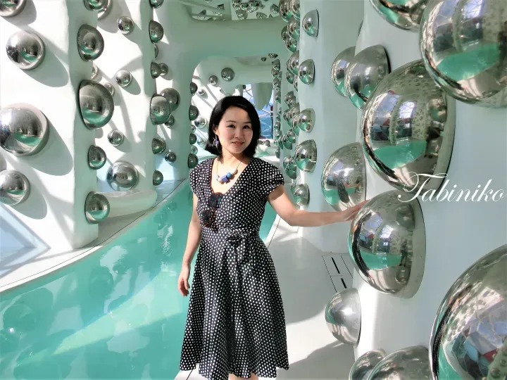 Woman in polka dot dress posing beside a pool at a modern property with metallic sphere decorations.