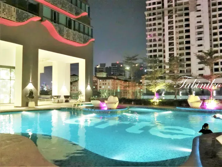 Night view of a modern swimming pool with blue lighting and lounge chairs at a Kuala Lumpur property.