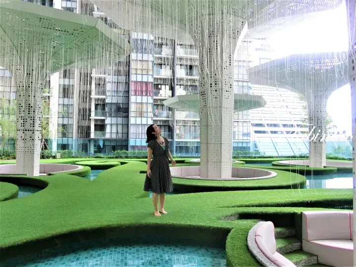 Woman in polka-dot dress standing on artificial grass in a modern garden with hanging fiber optic lights and water features.