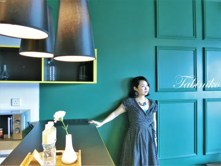 Woman in polka dot dress standing in modern kitchen with teal walls and pendant lights