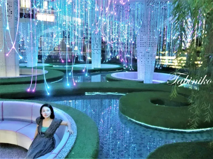 Woman sitting on a curved sofa in a modern lobby with glowing fiber optic lights and water features.