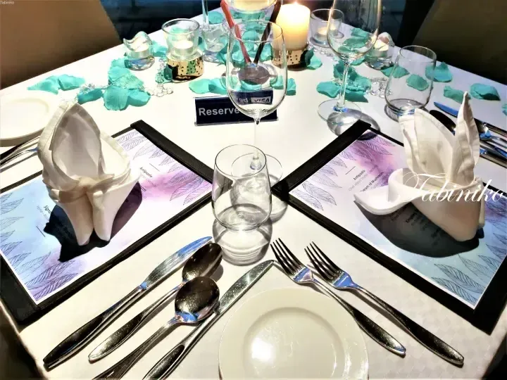 Elegant table setting with white linens, teal rose petals, and candles at a fine dining restaurant.