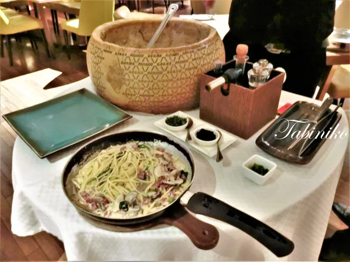大きなグラナ・パダーノチーズの輪と調味料を添えた、レストランのテーブルに置かれたスキレットのクリームパスタ