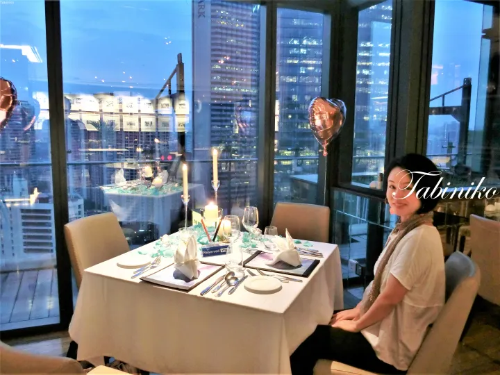 ザ・パークホテル・クアラルンプールの窓際で、キャンドルと都市の夜景を眺めながら食事をする女性。