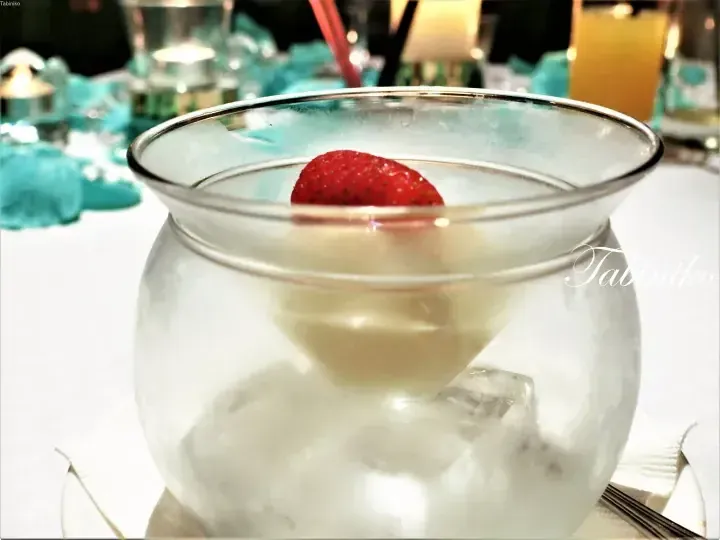 A creamy dessert in a glass bowl with a strawberry garnish, served over ice in a fine dining setting.