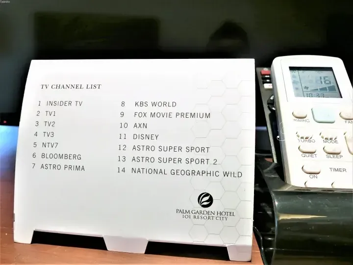 TV channel list card for Palm Garden Hotel IOI Resort City alongside an air conditioning remote control.