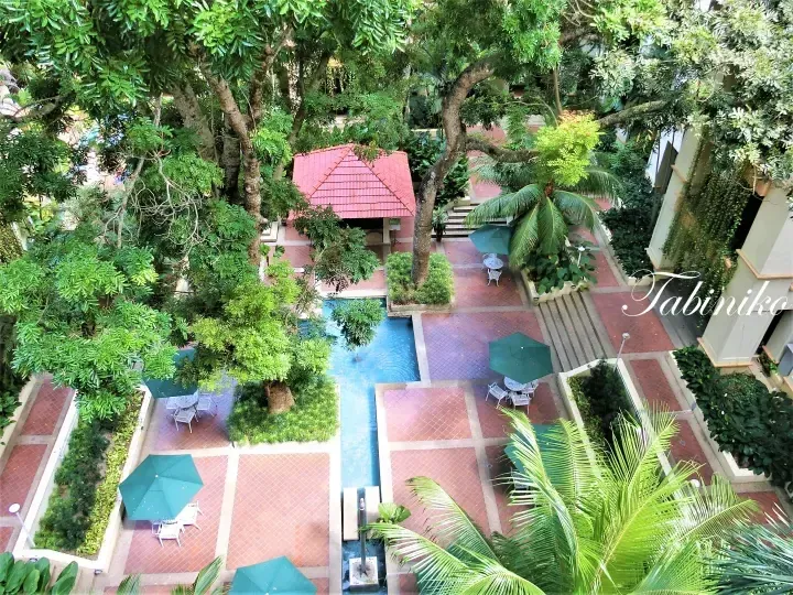 Aerial view of a lush tropical courtyard with a swimming pool, green umbrellas, and a red-roofed pavilion.