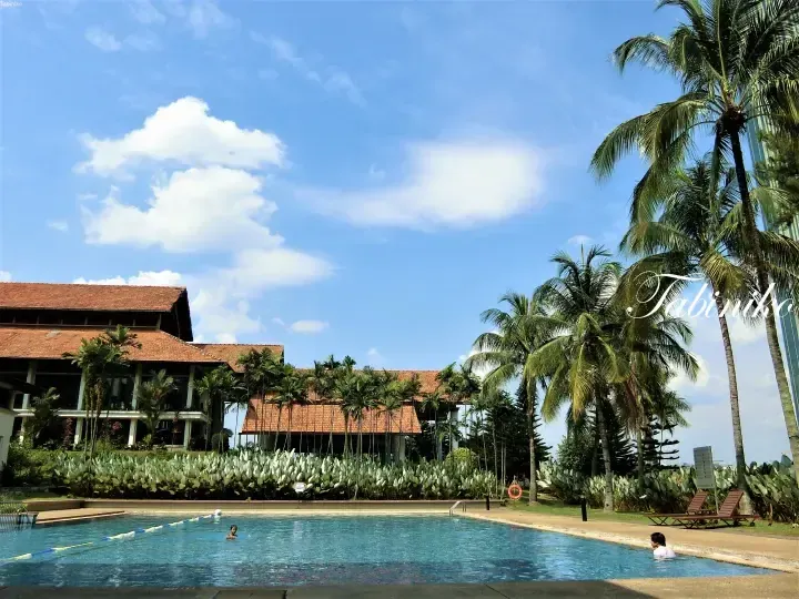 Outdoor swimming pool at a resort with palm trees and a building featuring a terracotta roof under a blue sky