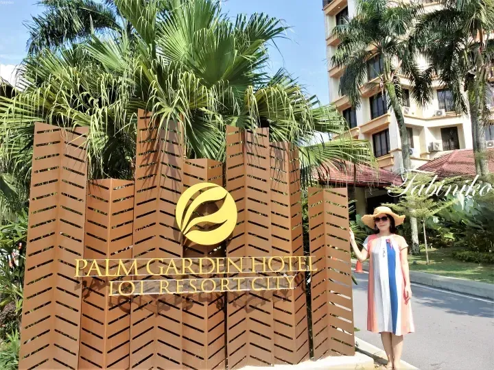 Woman in a straw hat posing next to the Palm Garden Hotel sign at IOI Resort City.