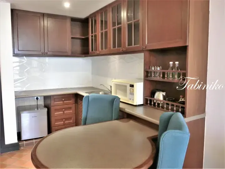 Compact kitchenette with wooden cabinets, Hisense mini fridge, microwave, and round dining table with blue chairs.