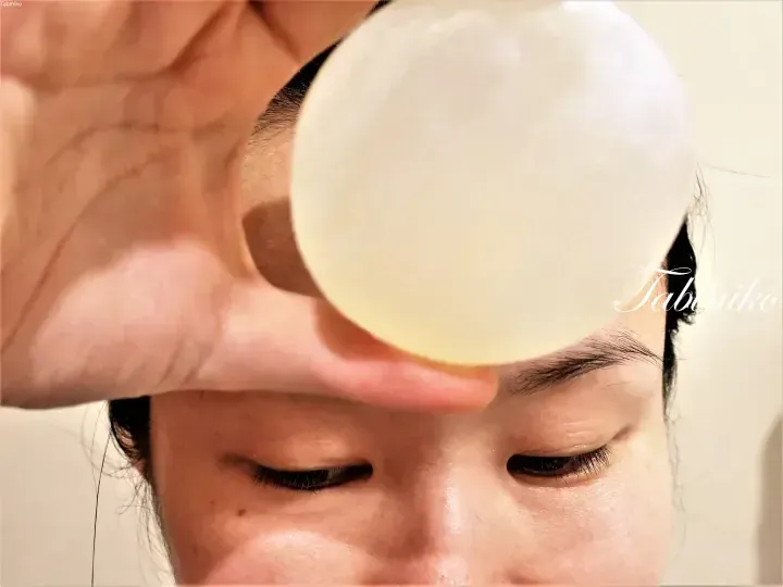 A close-up of a person holding a translucent circular object near their face, with the watermark Tabiniko visible.