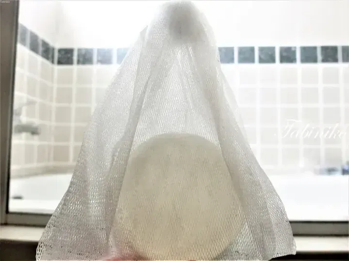 White mesh food cover draped over a bowl on a kitchen windowsill, with tiled wall in background.