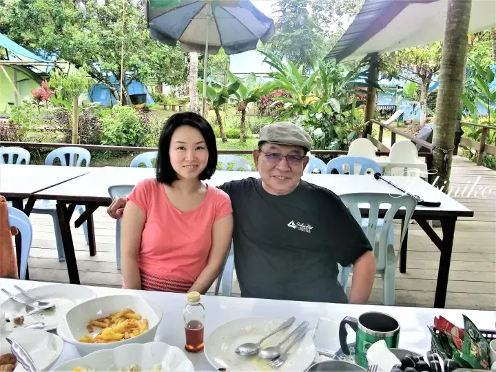 A smiling couple dining outdoors at Sailai Resort, surrounded by lush greenery and tents.