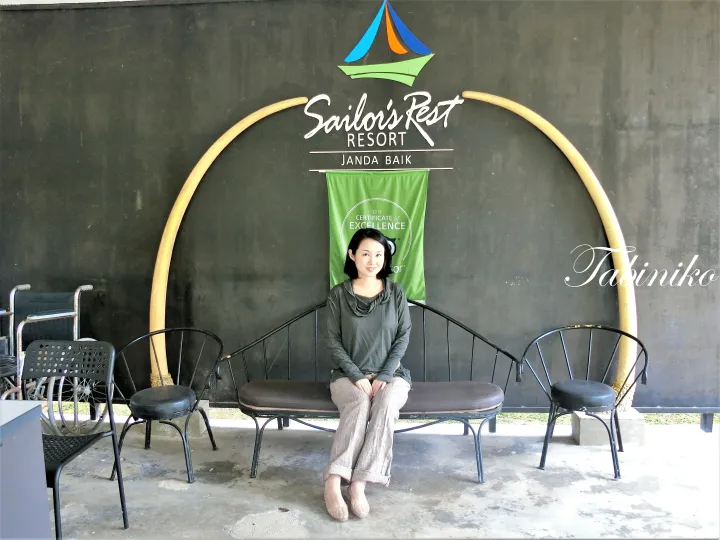 TripAdvisor優秀証書を背景に、Sailor&rsquo;s Rest Resort Janda Baikのベンチに座る女性。