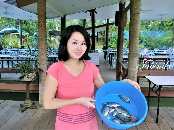 Woman in pink dress holding blue basin of fresh fish on wooden deck at Tabiniko resort