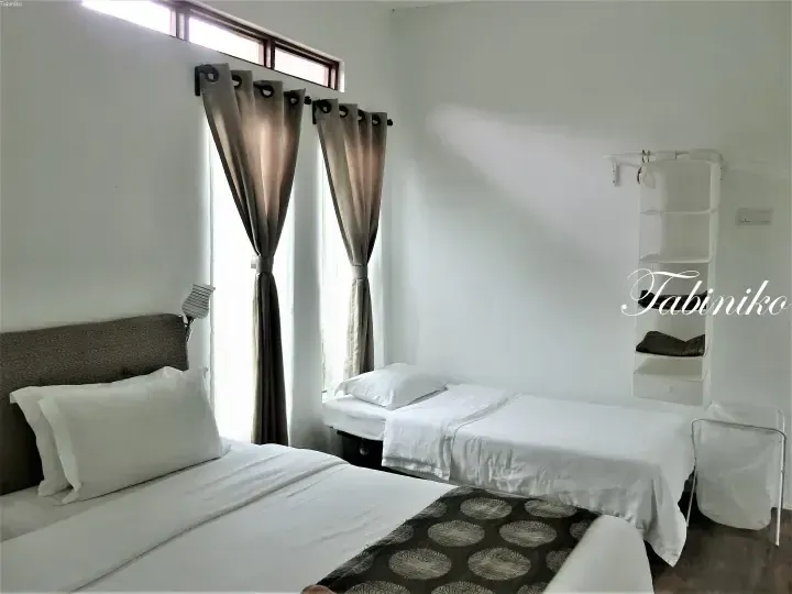 Bright hotel room with two single beds, white linens, and tall windows with beige curtains.