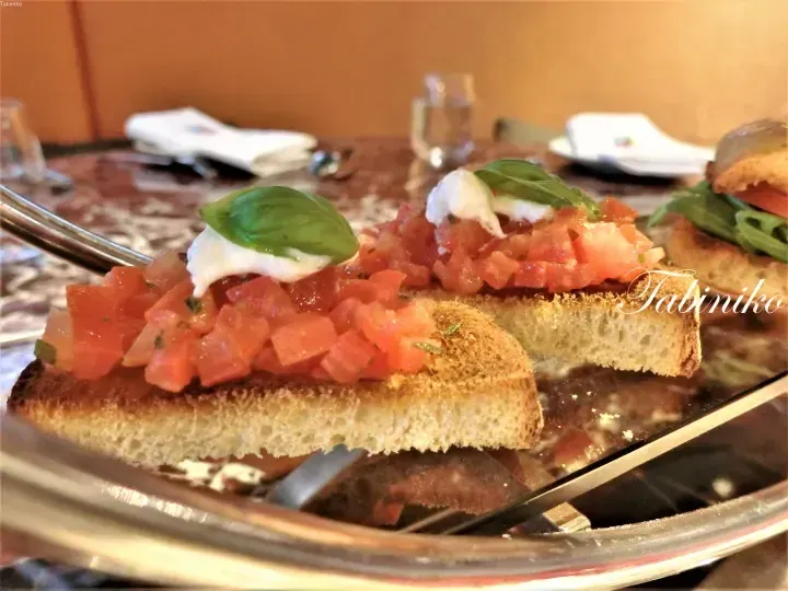 Bruschetta with diced tomatoes, fresh basil, and creamy topping served on toasted bread at a restaurant.
