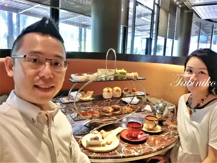 A couple enjoys afternoon tea at a restaurant, featuring a three-tier stand with savory sandwiches and sweet pastries.