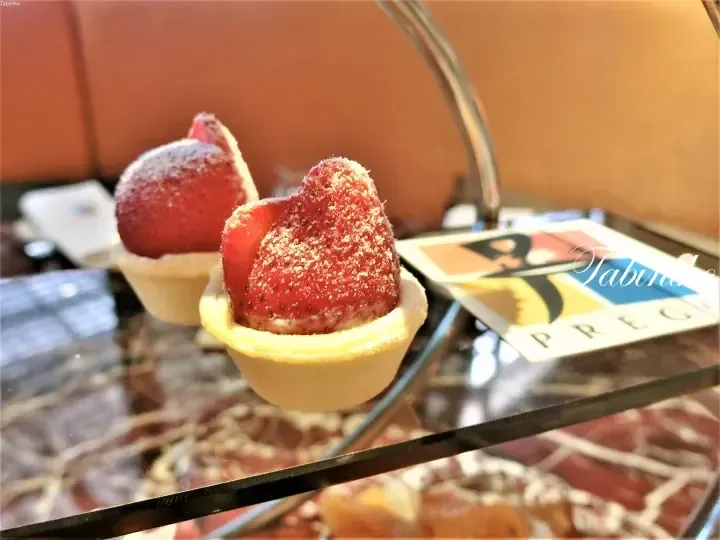 Close-up of two strawberry tarts dusted with sugar on a tiered stand, with a menu card visible in the background.