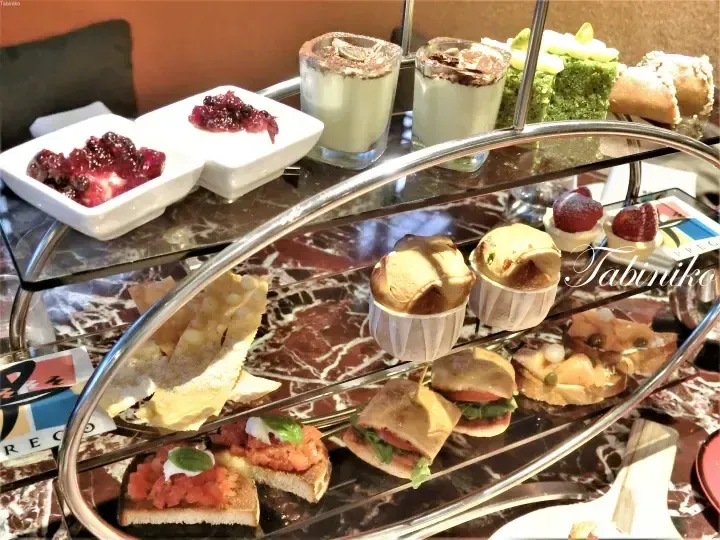 Three-tiered afternoon tea stand with savory sandwiches, pastries, and desserts.