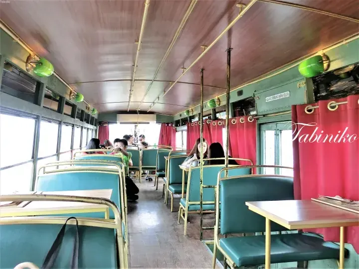 Interior of a vintage train carriage cafe with teal seats, brass fixtures, and red curtains at a Malaysian location.