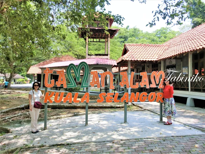 自然公園の入り口にある「Taman Alam Kuala Selangor」の看板の前でポーズをとる二人の女性。