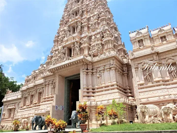 Ornate Hindu temple gopuram with intricate carvings and elephant statues at the entrance under a blue sky.