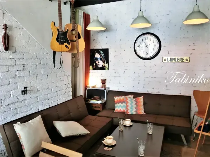 Cozy cafe interior with brown leather sofa, guitars on white brick wall, and Lumiere sign.