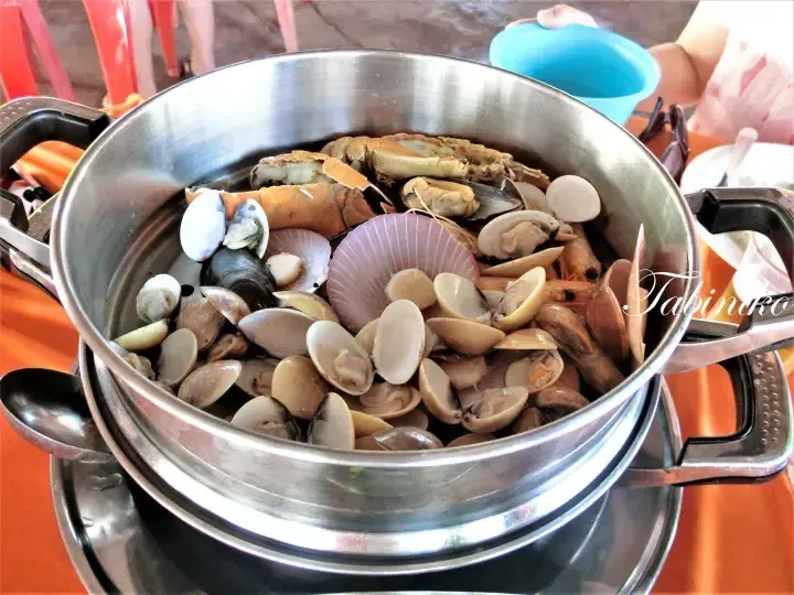 A stainless steel pot filled with steamed seafood including clams, scallops, mussels, and crab.