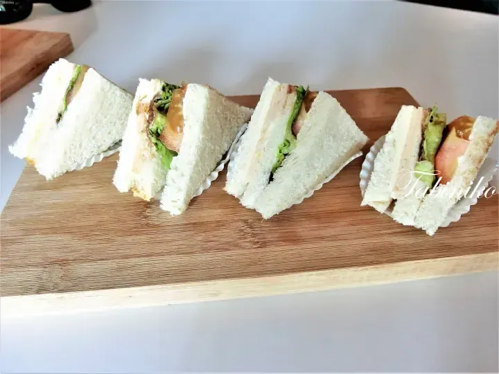 Four triangular club sandwiches with lettuce, tomato, and cheese arranged on a wooden board.