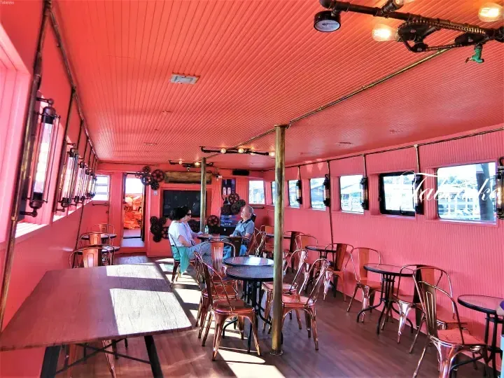 Interior of a cafe with vibrant pink walls, industrial-style lighting, and metal chairs.