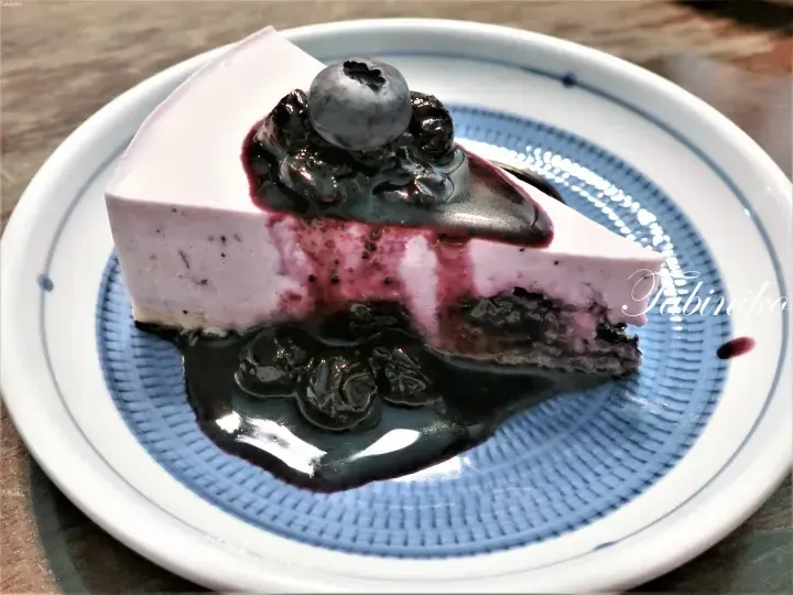 Slice of blueberry cheesecake with berry sauce and fresh blueberries on a blue and white patterned plate