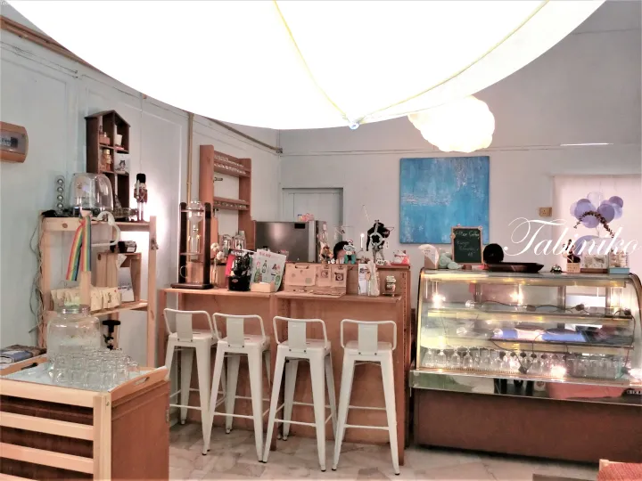 木製カウンターと白いバースツール、ガラスケースが並ぶ落ち着いたカフェの店内。