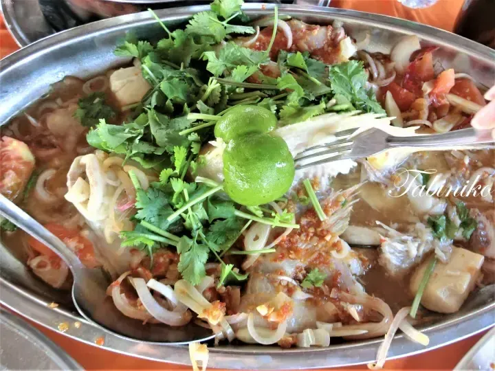 A steaming seafood hot pot with lime, cilantro, and chili sauce served in a metal bowl.