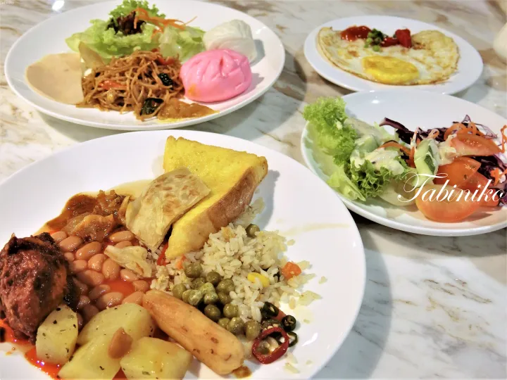 ナシレマック、ロティチャナイ、目玉焼き、蒸しパン、新鮮なサラダなど、豪華な朝食ビュッフェの盛り合わせ。