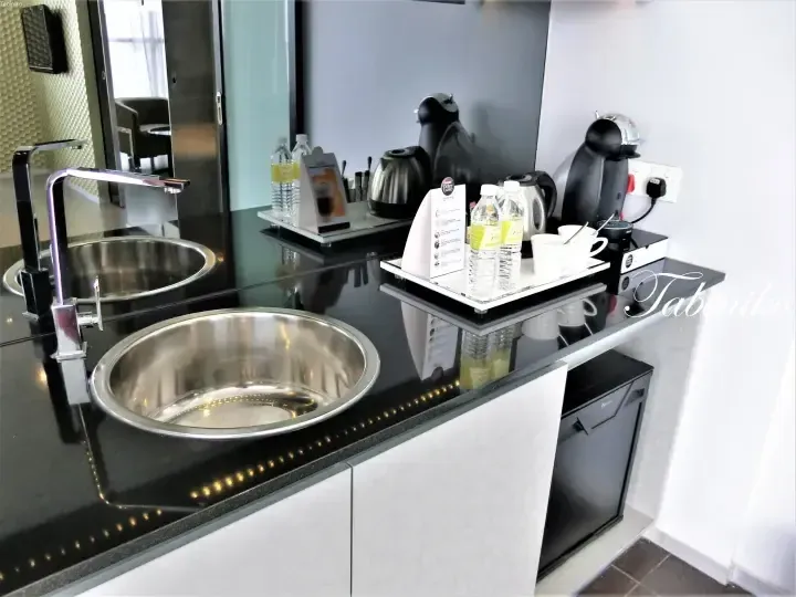 Modern hotel minibar area with a stainless steel sink, Nescafe Dolce Gusto machine, and complimentary bottled water.