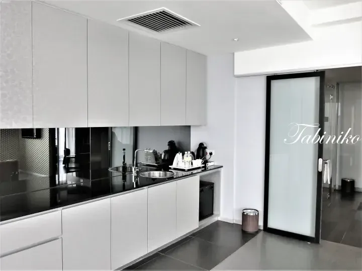 Modern kitchenette with white cabinets, black countertop, sink, and Nespresso machine in a hotel suite.