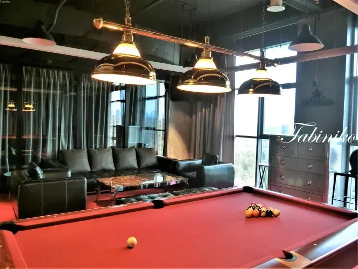 Modern lounge with a red pool table, black leather sofa, and large windows overlooking the city.