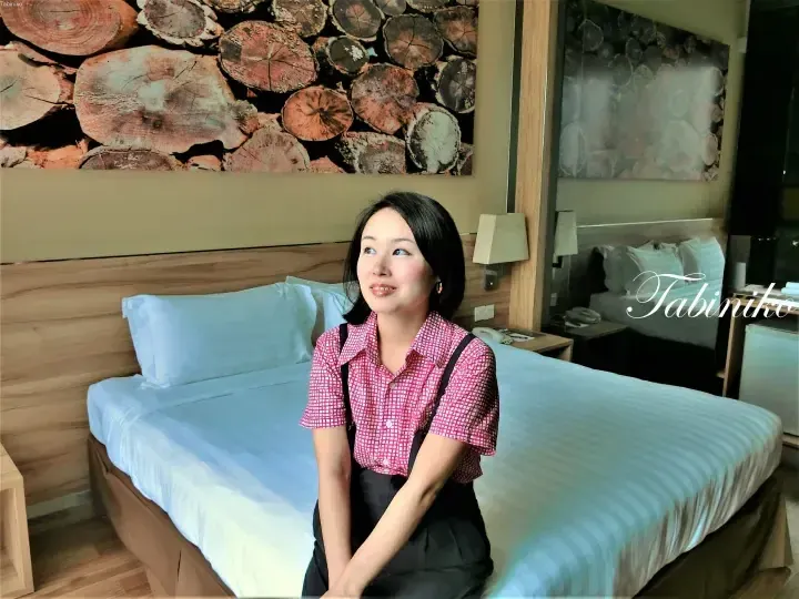 Woman sitting on a hotel bed with wood-themed wall art, showcasing a cozy room interior.