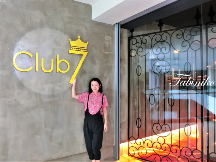 マレーシアのモダンな物件の入り口で、黄色いClub 7の看板の横に立つ女性。