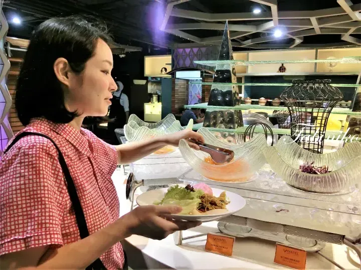 A woman selects salad ingredients at a buffet station in Vivatel Kuala Lumpur, featuring glass bowls of carrots and red cabbage.