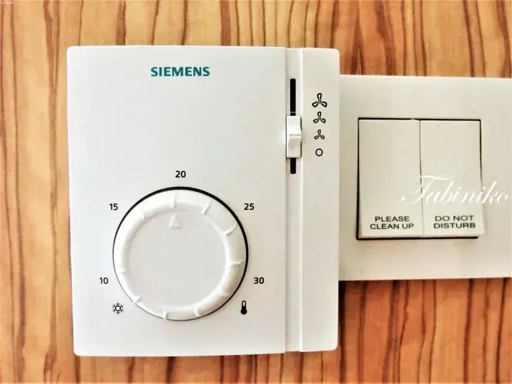 Siemens thermostat with fan speed controls next to a Please Clean Up and Do Not Disturb switch panel in a hotel room.