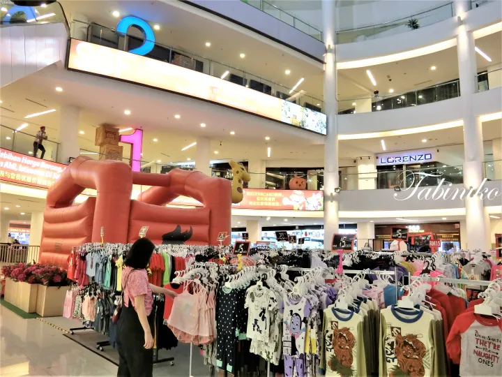 大きな赤いインフレータブルとSSFの看板があるショッピングモールのアトリウムに並ぶ子供服のラック。