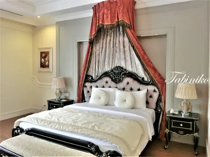 Luxurious bedroom with ornate black bed frame, plush tufted headboard, and dramatic red and gold canopy drapes.