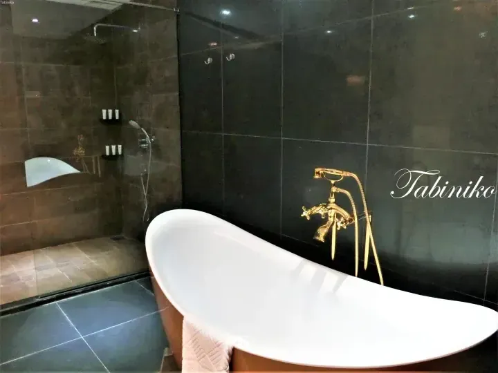Luxury bathroom with freestanding white bathtub and gold faucet against dark tiled walls