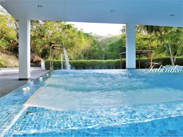 Outdoor swimming pool with water jets at a resort surrounded by lush greenery